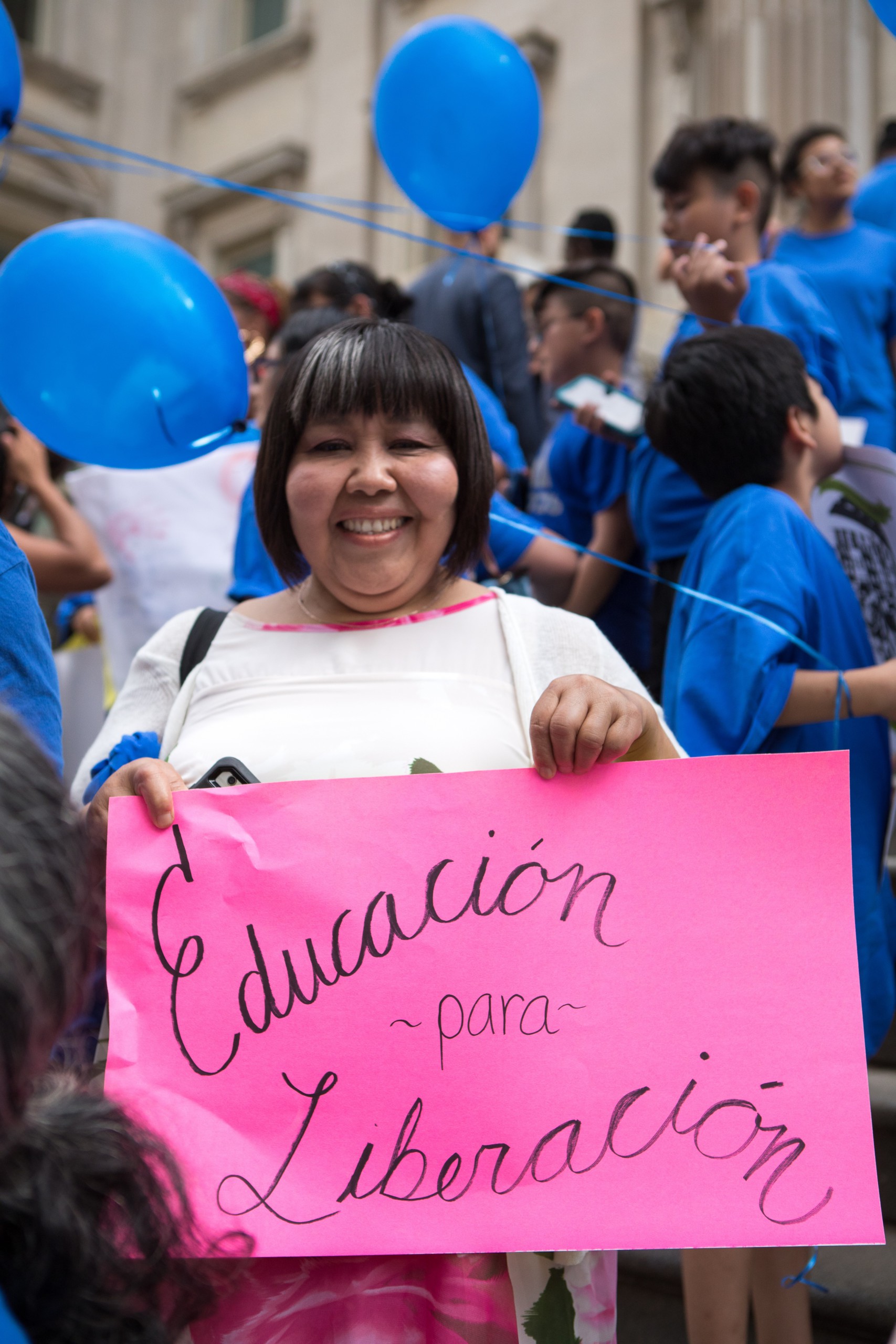A smiling demonstrator holds up a sign that reads, "Educacion para liberacion," during a NYC Coalition for Educational Justice rally.