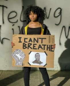 A young woman holds up a sign reading, "I can't breathe,' with an image of the Black Lives Matter fist logo and George Floyd. 