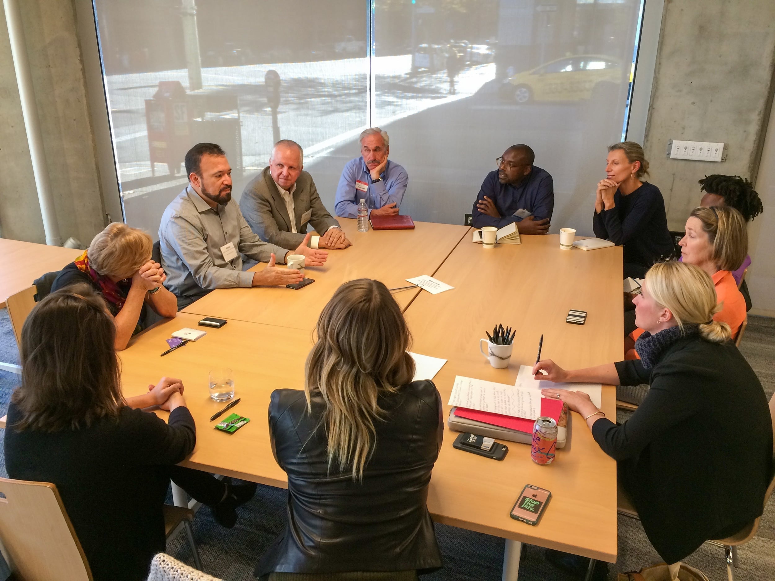 A racially and gender-diverse group of eleven people meeting around a large table at Google’s Community Space. 