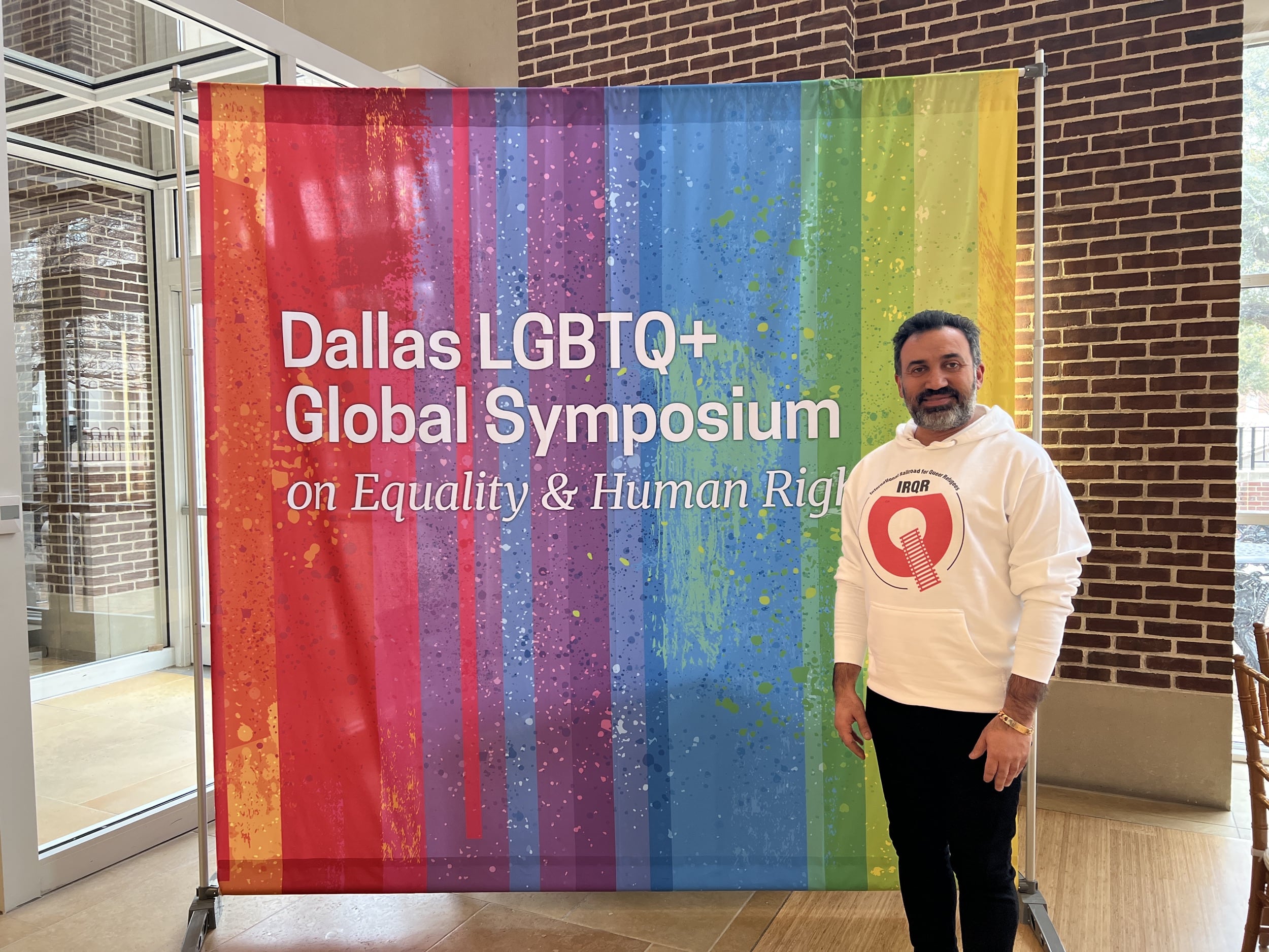 Arsham Parsi standing in front of a rainbow banner at the Dallas LGBTQ+ Global Symposium on Equality and Human Rights