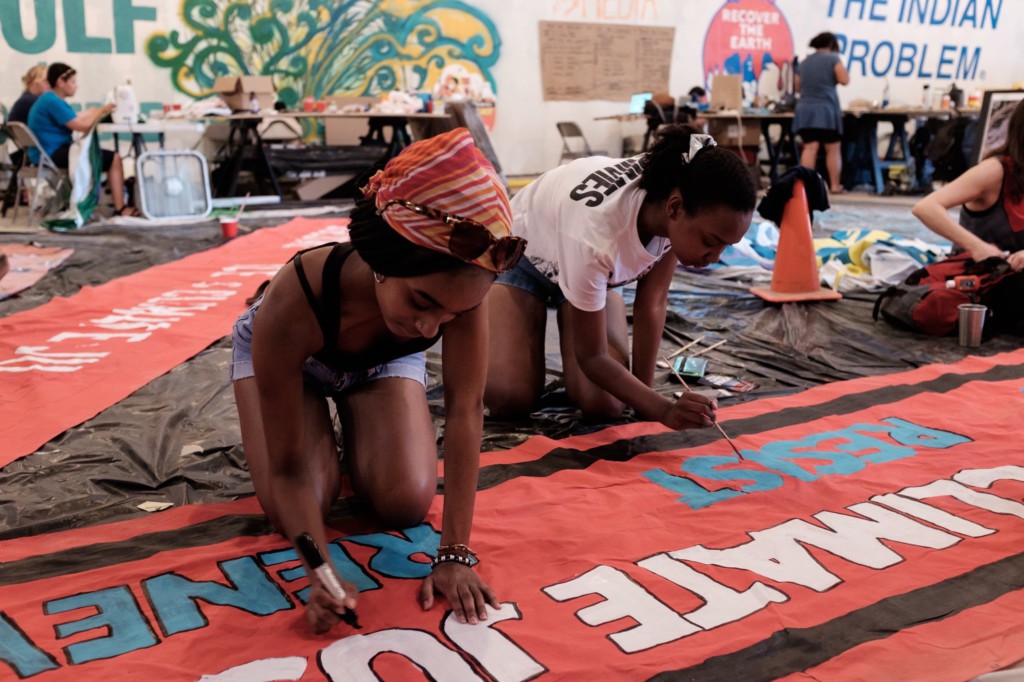 two women creating a red banner with the text "climate justice" in partial view