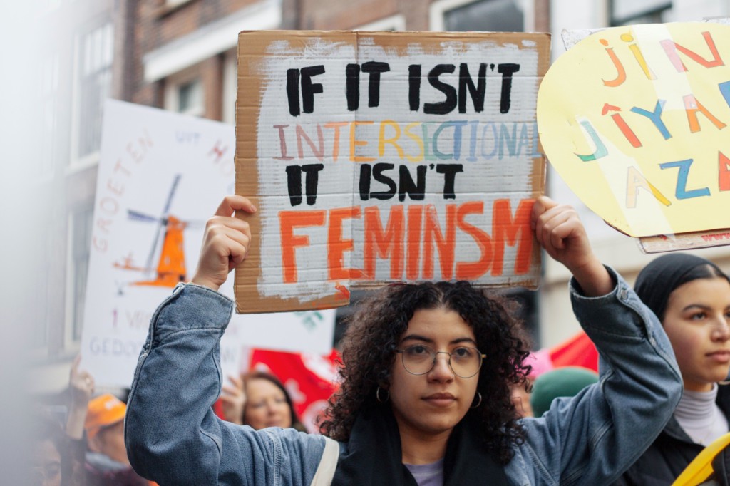 a woman holding up a sign that says "if it isn't intersectional it isn't feminism"