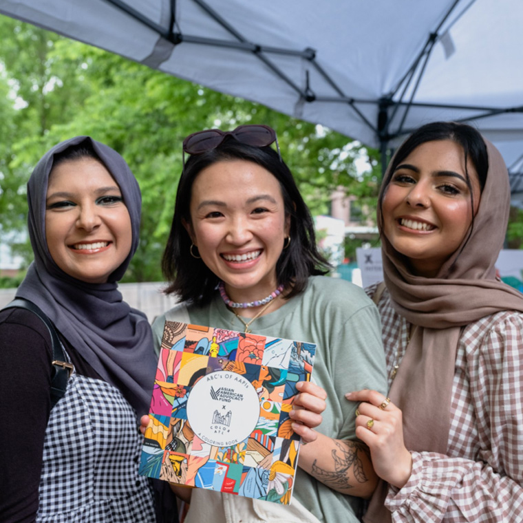Three AAPI women with the Asian American Advocacy Fund, a grantee of Tides’ I-Belong Fund, holding up a AAPI coloring book.