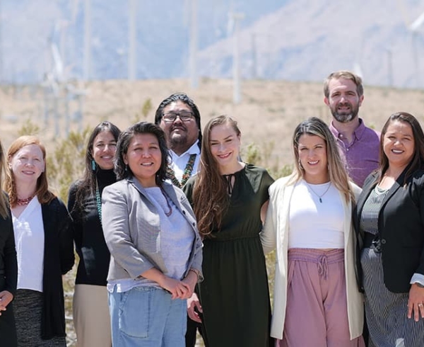 A multi-racial group of people working with Navajo Power, a fiscally sponsored partner of Tides, standing in front of wind turbines.