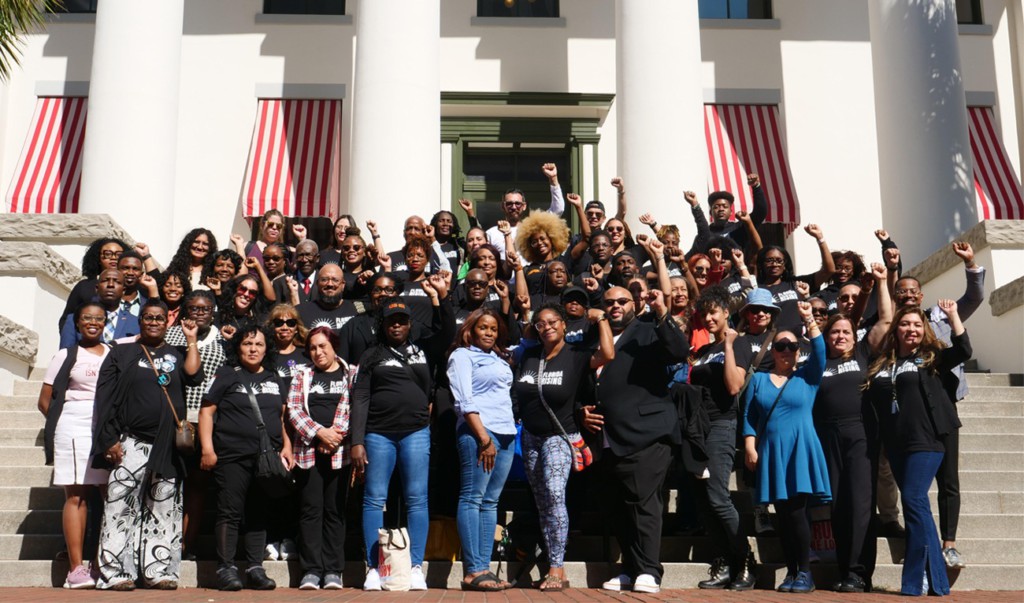 A large multiracial group of people standing together from Florida Rising, some people are raising their fists into the air.