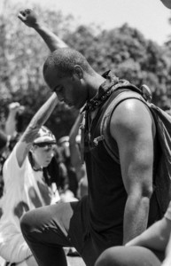 Side profile of a man kneeling with his right fist raised and head down.