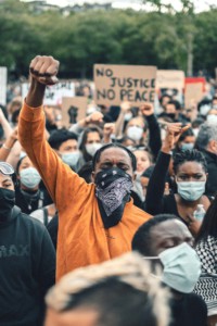 Man with his fist raised at a rally, with a sign in the background reading No Justice No Peace.