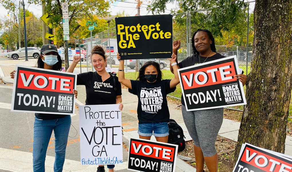 three people of color holding signs related to voting