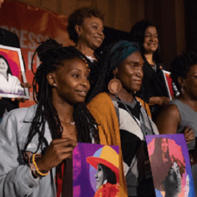 Black women at an event holding up posters of Black women leaders.