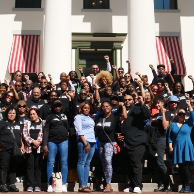 A large multiracial group of people standing together from Florida Rising, some people are raising their fists into the air.