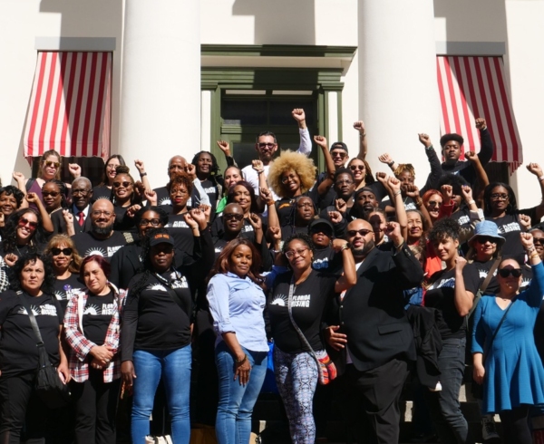 A large multiracial group of people standing together from Florida Rising, some people are raising their fists into the air.