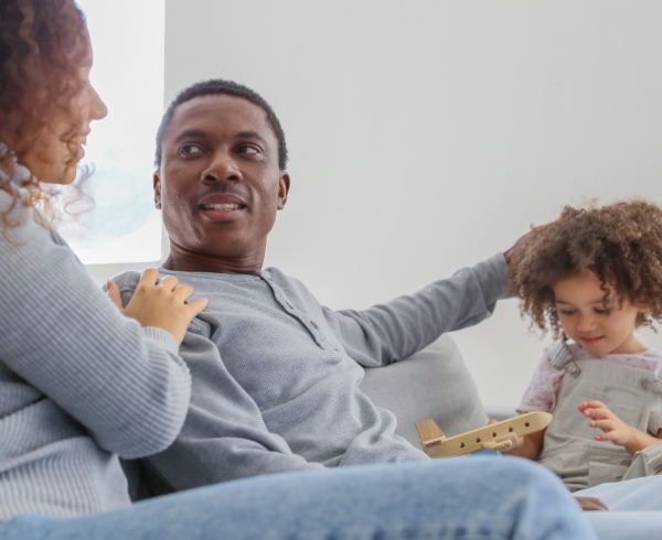 A Black family sitting on a couch together while the child plays with their toy.