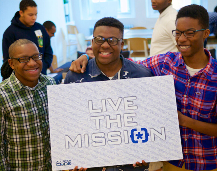 Three young Black men smiling and holding a sign that reads 'Live the Mission'. Photo credit: General Assembly, a fiscally sponsored project of Tides