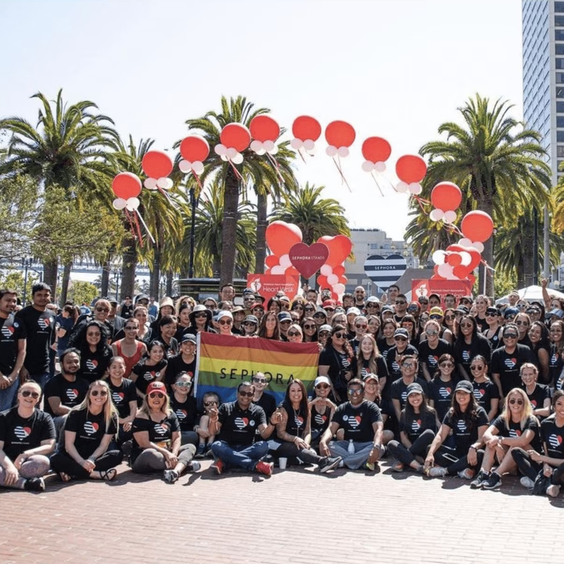 Large group of employees from Sephora with red balloons and a pride flag that has the word Sephora on it