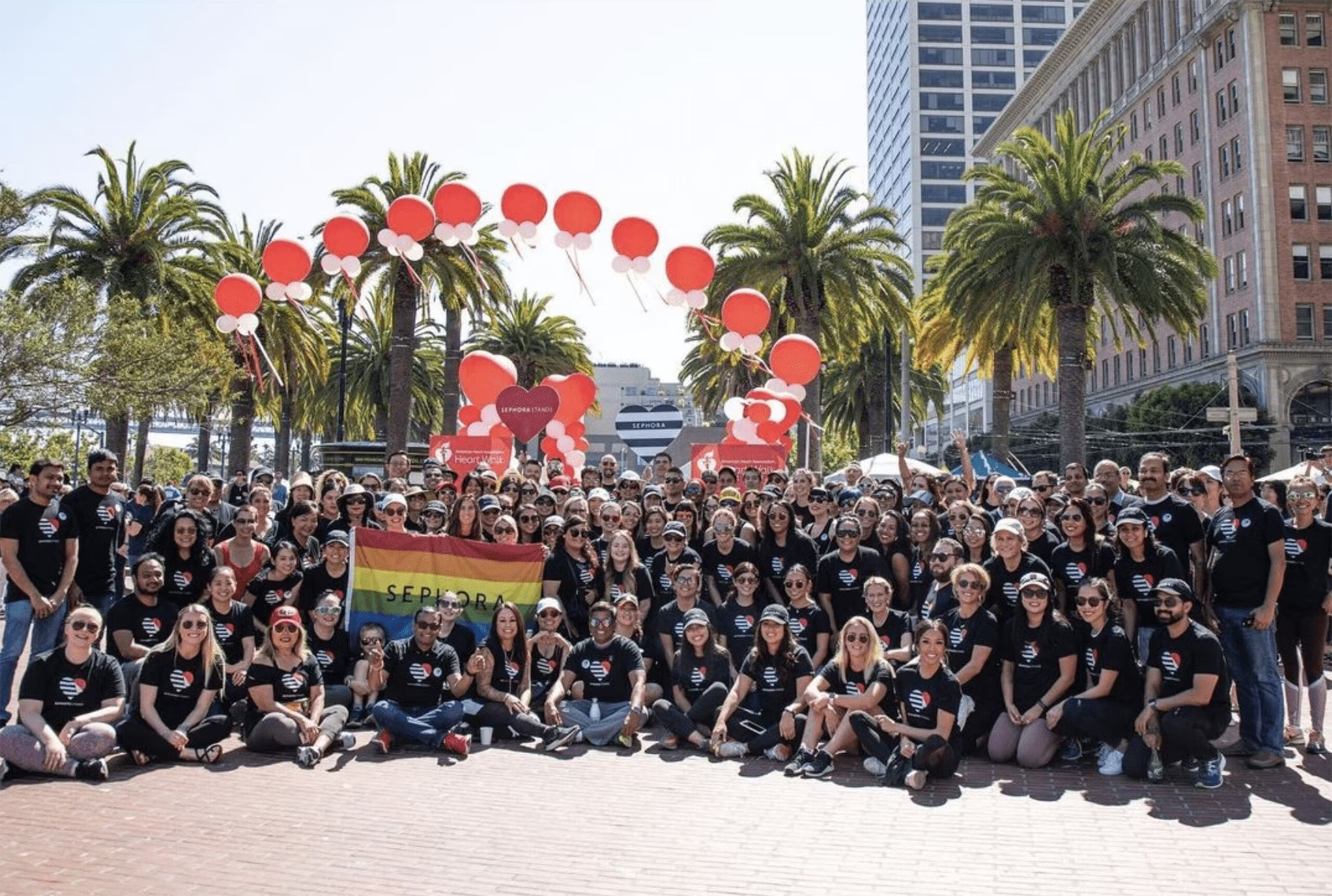 Large group of employees from Sephora with red balloons and a pride flag that has the word Sephora on it 
