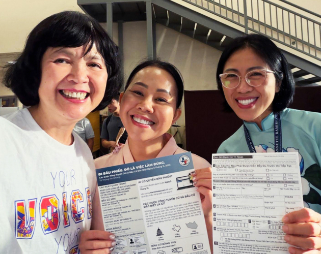 Three smiling community members in Houston hold Vietnamese-language voter registration forms and information about the November 2026 election.
