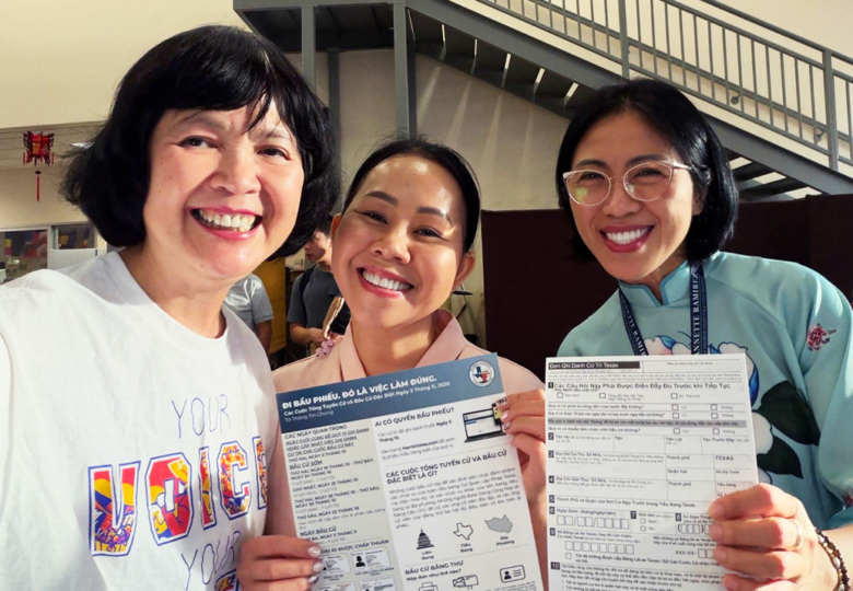 Three smiling community members in Houston hold Vietnamese-language voter registration forms and information about the November 2026 election.
