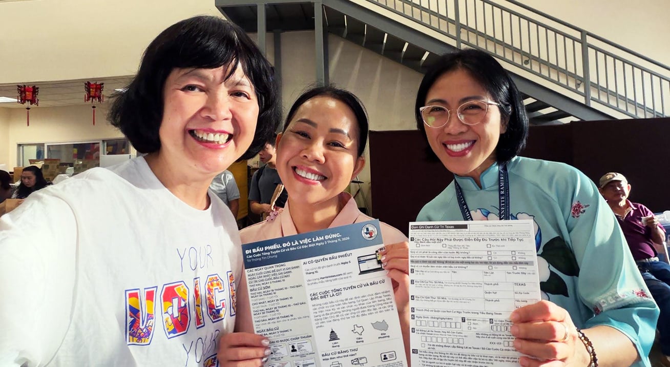 Three smiling community members in Houston hold Vietnamese-language voter registration forms and information about the November 2026 election.